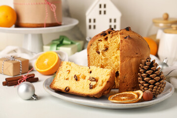 Plate with cut Panettone, cone, dried orange slices and Christmas decor on light background