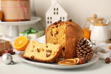 Plate with cut Panettone, cone, dried orange slices and Christmas decor on light background
