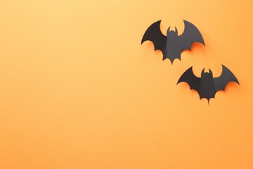 Fototapeta premium Halloween decor. Black paper bats on orange background, flat lay. Space for text