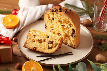 Plate with cut Panettone, vanilla sticks and Christmas decor on wooden background