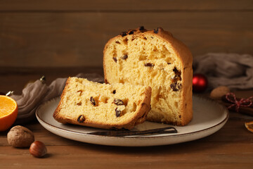 Plate with cut Panettone, vanilla sticks and nuts on wooden background