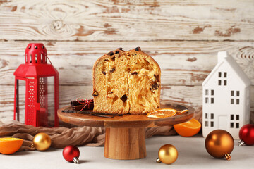 Stand with cut Panettone, dried orange slices, Christmas balls, cinnamon and vanilla sticks on light table against wooden wall