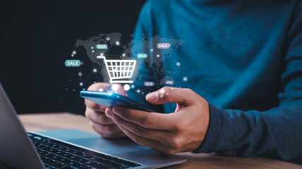 Person using smartphone with shopping cart icon and sale tags overlay near laptop on a wooden surface