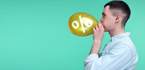 Man blowing golden balloon with percent sign on turquoise background. Discount offer