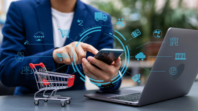 Man using smartphone for online shopping with laptop and shopping cart on desk with digital icons overlay