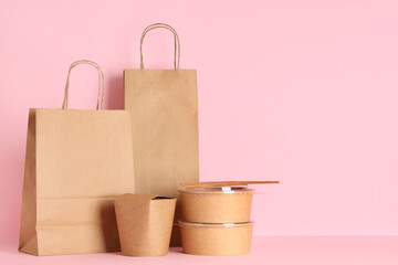 Paper bags with containers and chopsticks on pink background