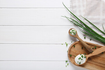Cutting board with spoons of tasty sour cream and fresh green onion on white wooden table