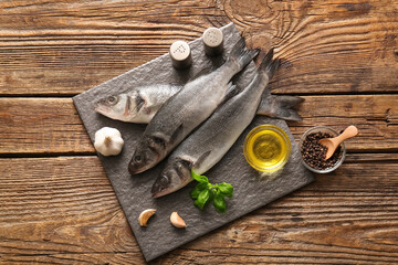 Board with fresh raw seabass fishes and different spices on wooden background