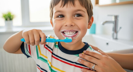 Happy child brushing teeth with toothbrush in bathroom while smiling. Child enjoys good dental hygiene with colorful striped shirt and toothpaste on brush. Concept of daily oral care for kids.