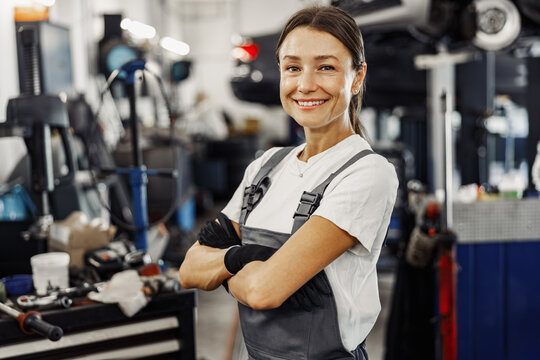 A confident woman mechanic stands proudly and poses in an auto repair workshop environment filled with tools