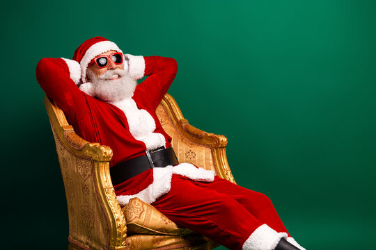 Stylish Santa Claus relaxing in a luxurious golden chair wearing sunglass during the festive Christmas season on a green background