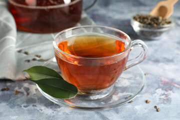 Cup of tasty black tea and green leaves on blue grunge background, closeup