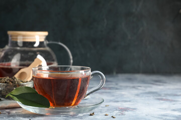 Cup of tasty black tea and green leaves on blue grunge background