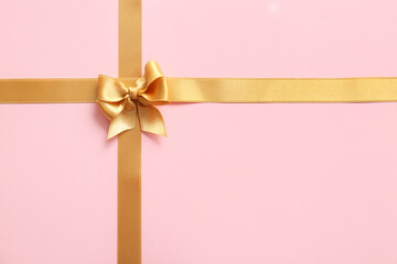 Fototapeta premium Bow made of golden satin ribbons on pink background