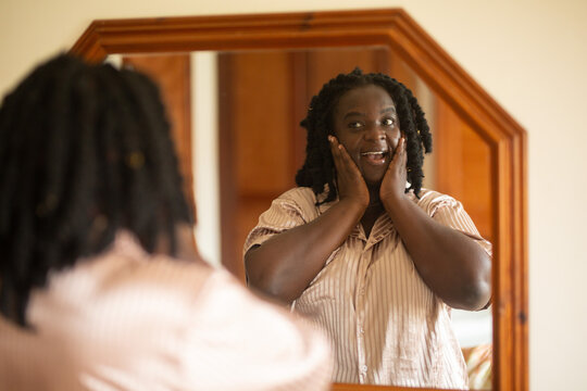 Happy Black woman with natural hair looking at her reflection in the mirror with a surprised and joyful expression