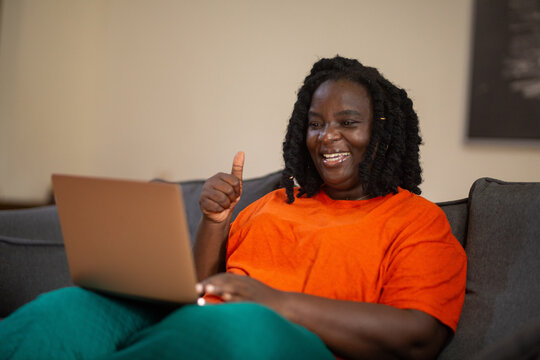 Happy Black woman gives a thumbs up in approval during a successful video call on her laptop from her couch