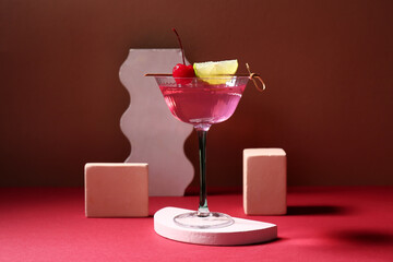 Plaster podiums, glass of tasty Cosmopolitan cocktail garnished with lime slice and cherry on pink background