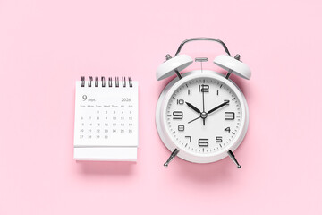 Calendar with alarm clock on pink background