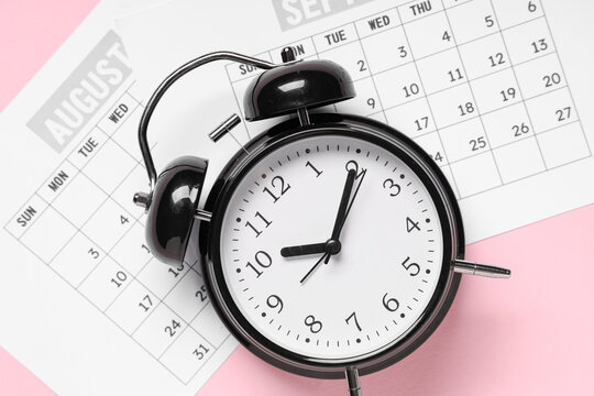 Calendar with alarm clock on pink background
