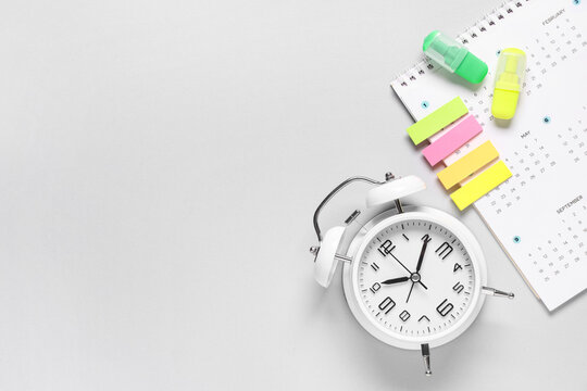 Calendar with alarm clock, markers and stickers on grey background