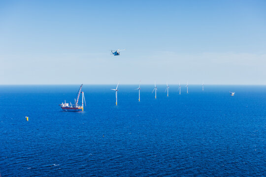Large helicopter flying over the Baltic Sea with landscape and wind farms in the background.