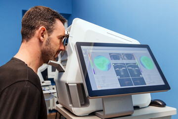 Male patient undergoing eye examination using advanced diagnostic equipment in a modern clinic,...