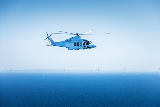 Large helicopter flying over the Baltic Sea with landscape and wind farms in the background.