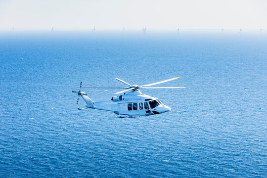 Large helicopter flying over the Baltic Sea with landscape and wind farms in the background.