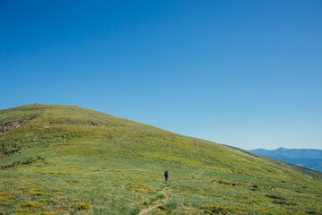 A woman hikes solo with a backpack on a sunny day and mountains on the background