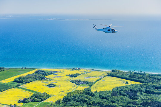 Large helicopter flying over the Baltic Sea with landscape and wind farms in the background.