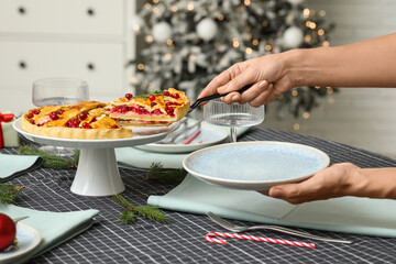 Woman taking piece of delicious cranberry pie in Christmas decorated room