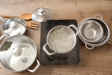 Cooking pot with boiling water and mini stove on table, top view