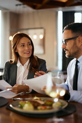 Smiling colleagues going through paperwork during business lunch in restaurant.