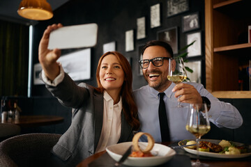 Cheerful coworkers taking selfie during business lunch in restaurant.