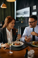 Happy coworkers using cell phone during business lunch in restaurant.