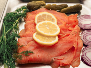 Serving of fine smoked salmon, fresh tomato, onion, gherkin, lemon and dill on a stainless steel plate. Beer food plate.