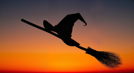 Silhouette of a witch's hat sitting on a broom against an orange twilight sky  
