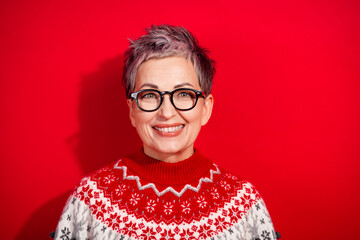 Stylish mature woman in festive sweater with red background radiates holiday cheer and happiness