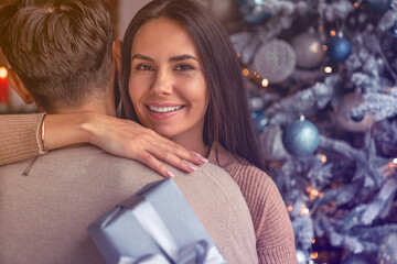 Young man and woman with a beautifully decorated gift box hugging near a Christmas tree. Gift...