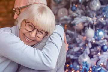 Senior couple hugging at home at Christmas time. Elderly old spouses grandparents embracing cuddling together celebrating winter holidays New Year Eve