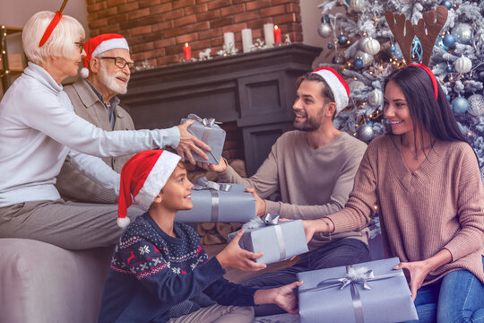 Happy three generation family sitting together in living room on Christmas eve and exchanging gifts. Happy New Year! Winter holidays spirit. Family reunion - Powered by Adobe