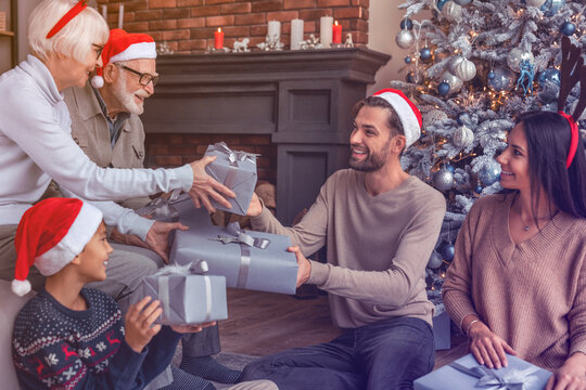 Happy family sitting near Christmas tree in living room exchanging christmas presents. Caucasian three generation family reunion. Gift sharing giving concept