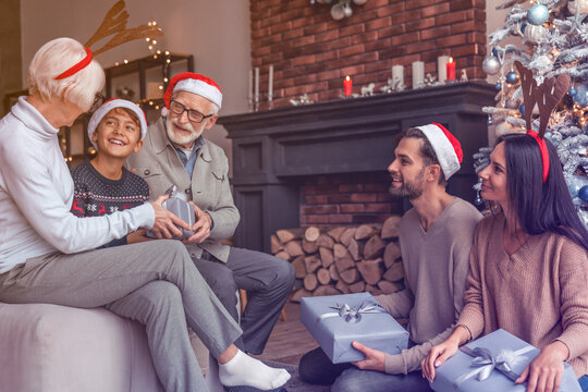 Happy young family sitting together in living room on Christmas eve and exchanging present boxes. Happy New Year Eve! Family reunion for winter holiday spirit