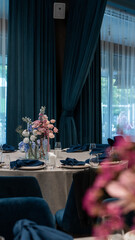 wedding decoration of a round table with a floral arrangement in blue and pink colors. Rose, delphinium, carnation, dahlia, eryngium, candles, blue napkins