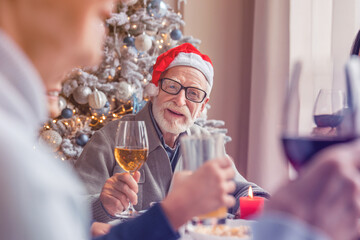 Senior smiling man enjoying christmas dinner together at home with his family toasting cheering for New Year with flutes glasses of sparkling wine champagne