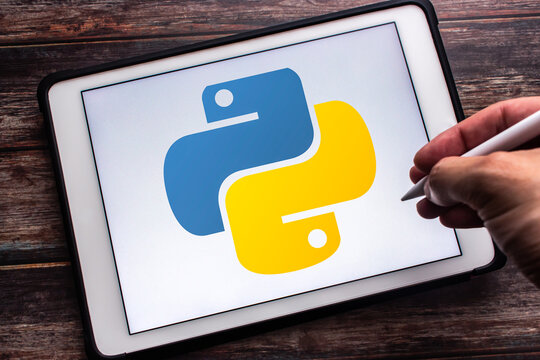 Quito, ECUADOR - Oct 14 2025 : Logo of Python on tablet on wooden table. Man hand holding wireless stylus pen