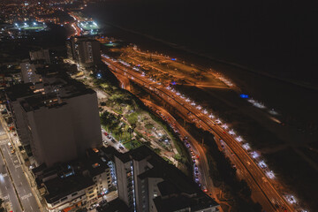 Aerial panoramic capturing urban night traffic flowing along a brightly lit coastal highway