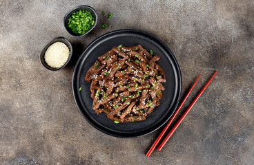 Stir-fry beef marinated with teriyaki sauce, green onions, and sesame seeds on a dark background. Top view