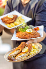 Waiter serving vegetarian and classic cordon bleu with potato salad and lemon garnish at an outdoor restaurant