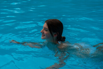 Naklejka premium A girl enjoys a refreshing swim in a clear, azure-blue swimming pool.